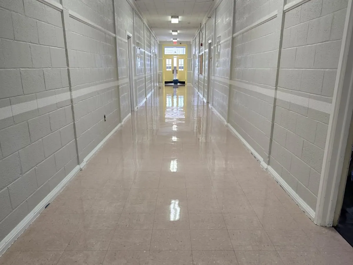 A long institutional corridor with painted block walls and a freshly polished tile floor reflecting the ceiling lights