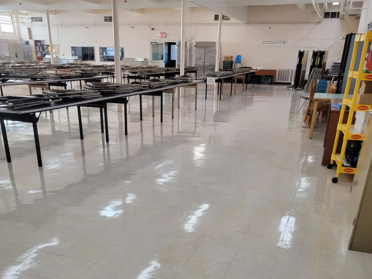 A school cafeteria with folding tables stacked to one side and a freshly stripped and refinished tile floor