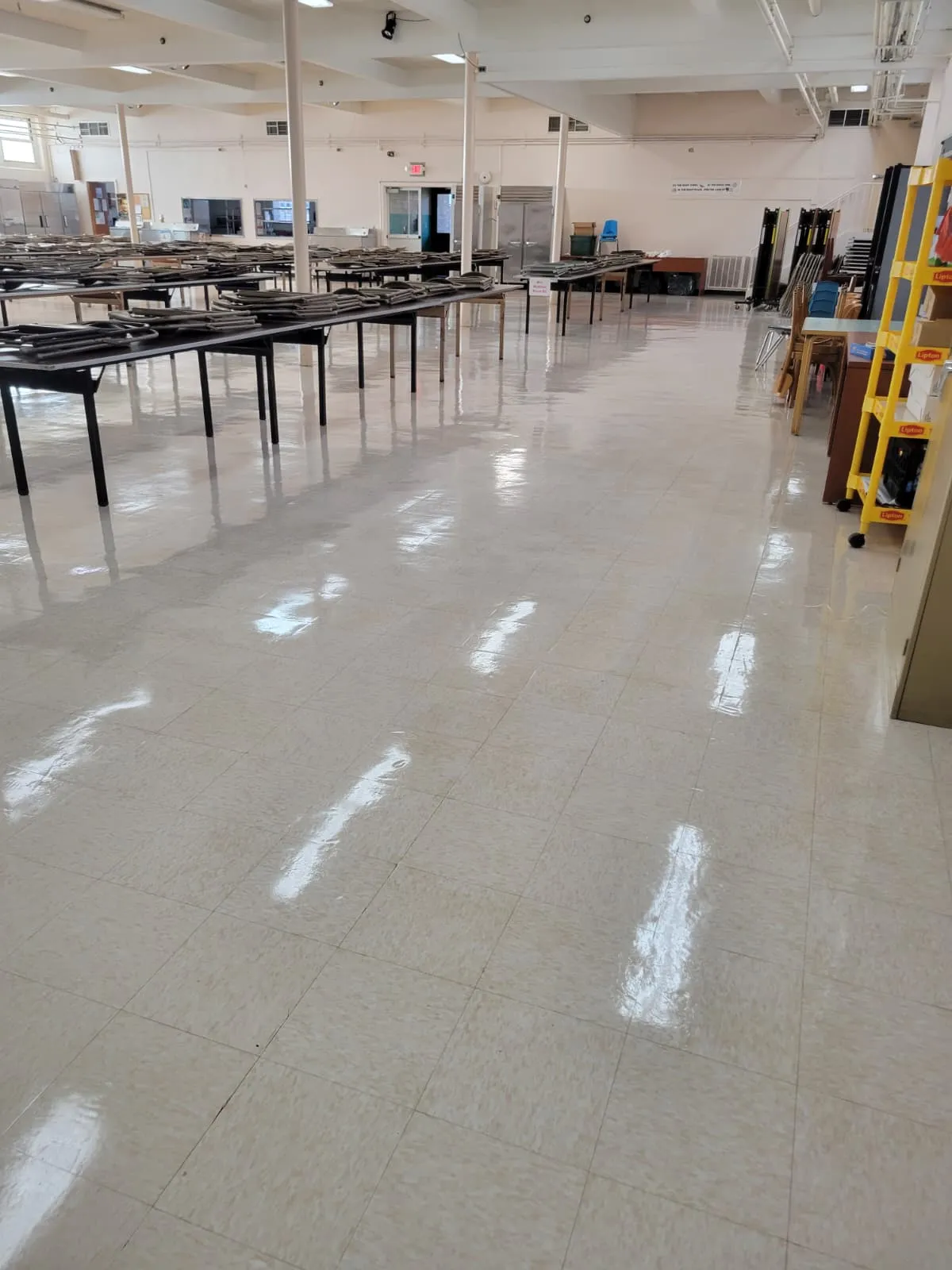 A school cafeteria with folding tables stacked to one side and a freshly stripped and refinished tile floor
