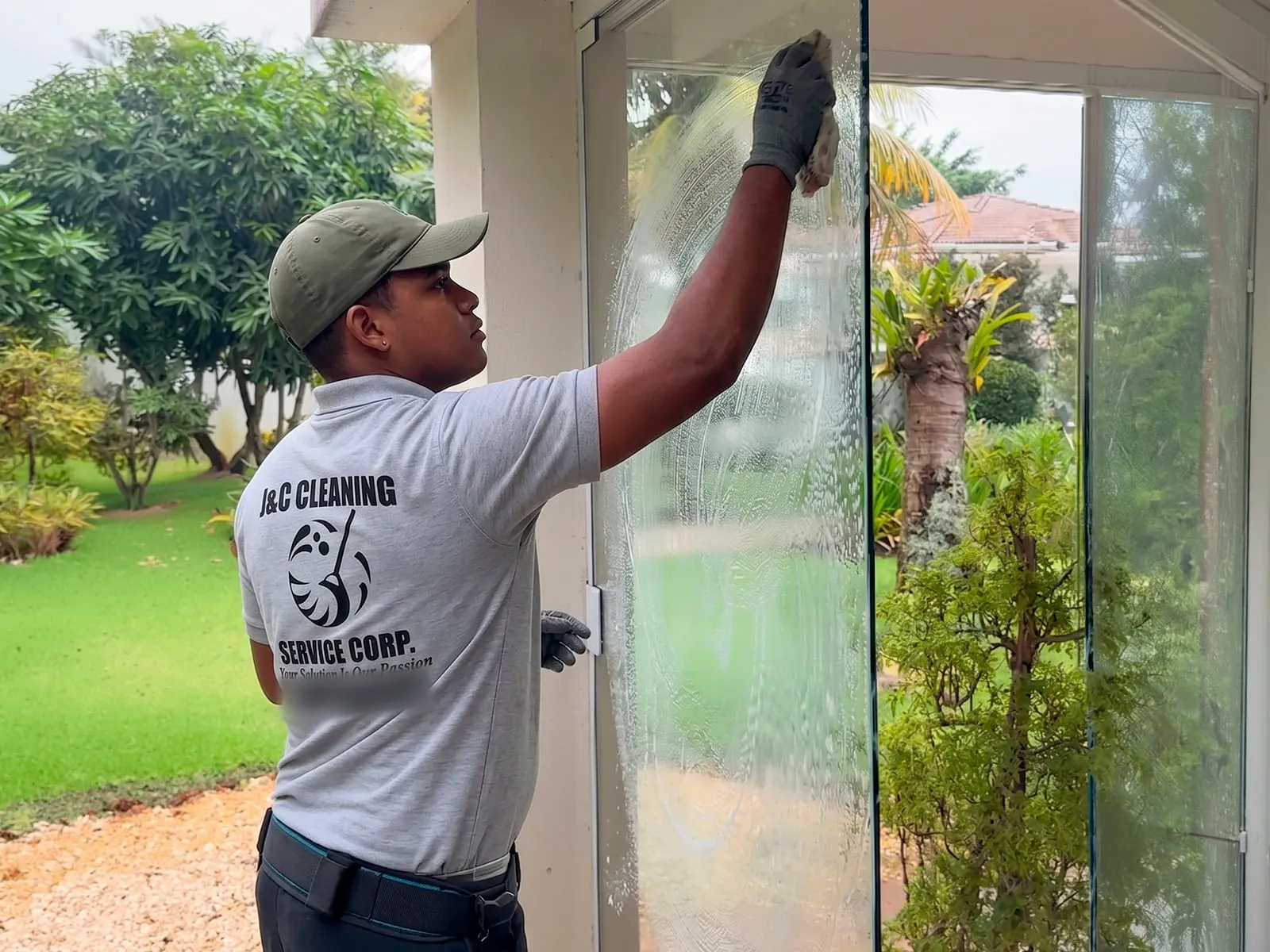 A J&C Cleaning Services technician in a branded polo and work gloves washing the glass of an entrance door