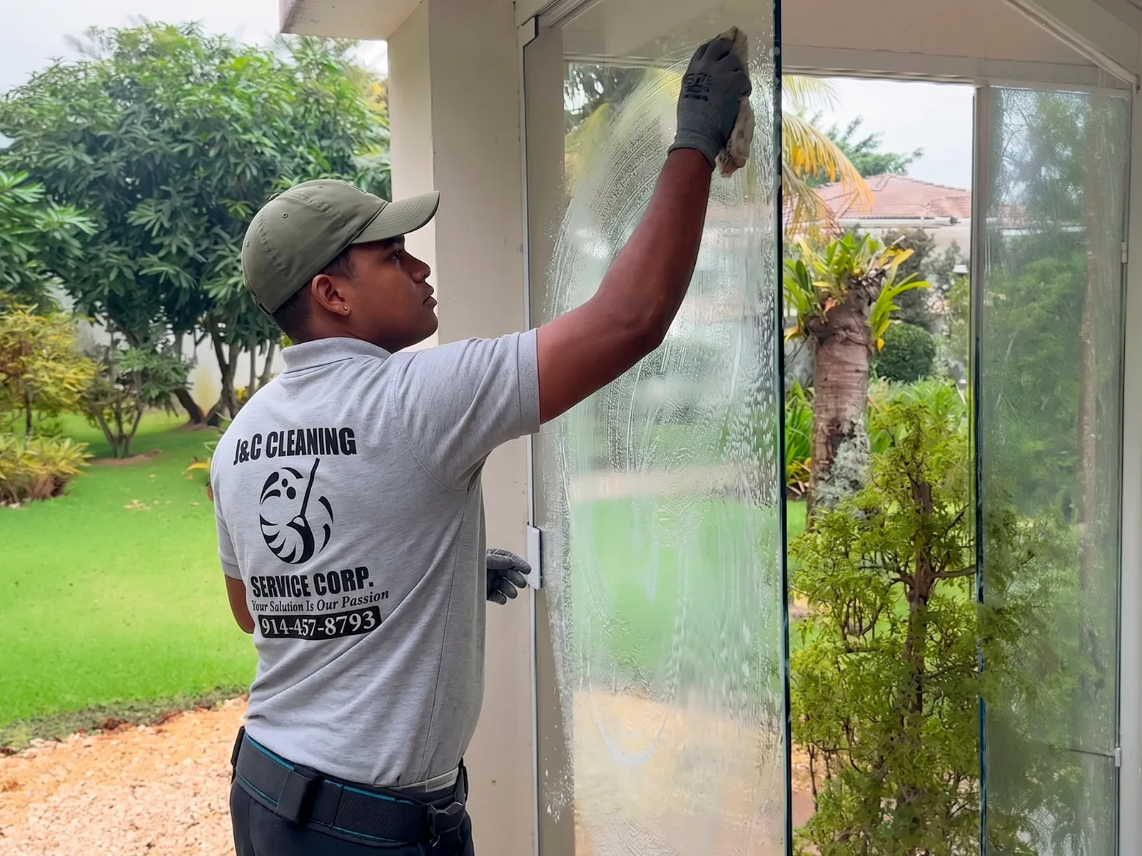 Un técnico de J&C Cleaning Services, con el polo corporativo y guantes de trabajo, limpiando el cristal de una puerta de entrada
